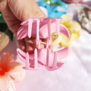 May include: A pink plastic hair claw with a flower-shaped design. The claw has four prongs on each side.