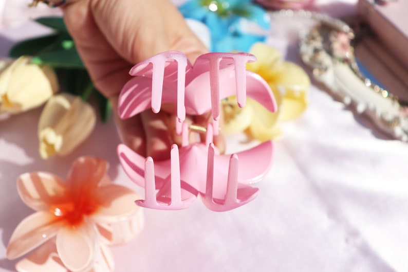 May include: A pink plastic hair claw with a flower-shaped design. The claw has four prongs on each side.