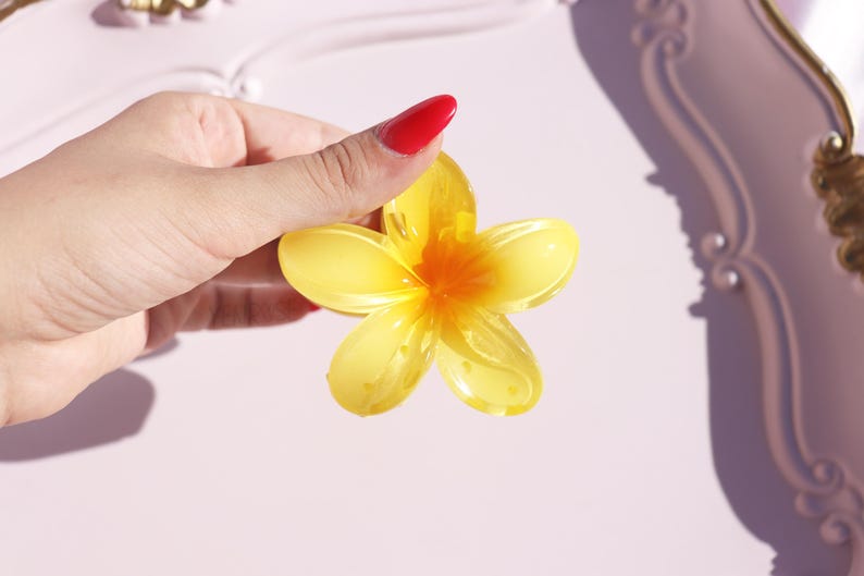 May include: A yellow resin flower with five petals and a center that is a darker yellow. The flower is held in a hand.