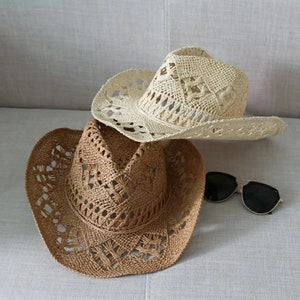 Puede incluir: Dos sombreros de vaquero de paja tejida. Uno es beige claro y el otro marr&oacute;n. Ambos tienen un patr&oacute;n de tejido abierto. Un par de gafas de sol negras con montura dorada descansa cerca de los sombreros.