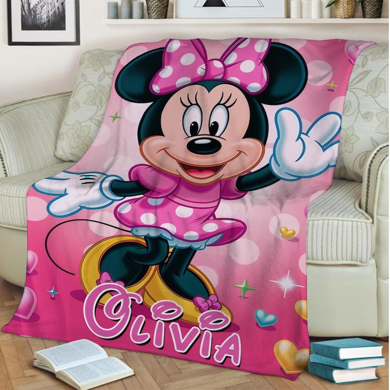 Puede incluir: Manta de forro polar rosa con un gran gr&aacute;fico de Minnie Mouse. Minnie lleva un vestido y un lazo rosa con lunares. La manta tiene el nombre "Olivia" impreso, junto con corazones y estrellas.
