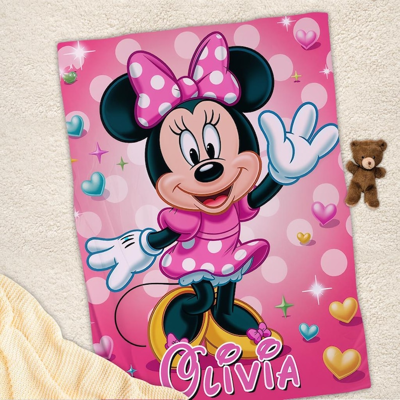 Puede incluir: Manta rosa de Minnie Mouse con un personaje grande de Minnie Mouse con un vestido y lazo de lunares rosas. La manta tiene un fondo rosa con lunares blancos, corazones y estrellas. El nombre "Olivia" est&aacute; escrito en rosa.