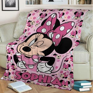 May include: Pink fleece blanket featuring Minnie Mouse with a large polka dot bow and the name "SOPHIA" in large pink letters. The blanket has a repeating pattern of Minnie Mouse and flowers.