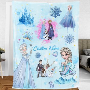 May include: A blue and white fleece blanket with a Frozen theme. It features images of Elsa, Anna, Olaf, and other characters from the movie. The blanket also has a custom name field.
