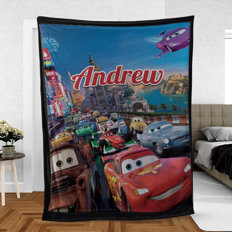 Op de afbeelding: Een zwarte fleece deken met een levendige sc&egrave;ne uit de animatiefilm Cars. De deken toont Bliksem McQueen en andere personages die door een stad racen, met de naam "Andrew" in rood script.