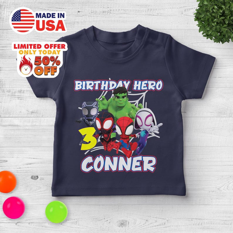 Puede incluir: Una camiseta de manga corta azul marino con un estampado gr&aacute;fico de cinco superh&eacute;roes de dibujos animados, incluidos Hulk, Spider-Man y Black Panther. El texto dice BIRTHDAY HERO, el n&uacute;mero 3 en amarillo y el nombre CONNER en letras blancas.