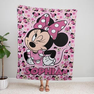 May include: Pink blanket featuring Minnie Mouse with a polka dot bow and dress. The blanket has a repeating pattern of Minnie Mouse and hearts. The name "SOPHIA" is printed in large pink letters at the bottom of the blanket.