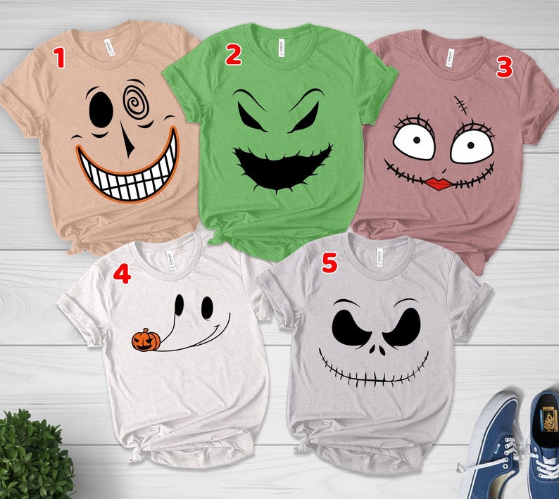 May include: Five short-sleeved t-shirts featuring character faces from The Nightmare Before Christmas. Shirt 1 is tan with a spiral eye, 2 is green with a jagged mouth, 3 is mauve with stitched eyes and lips, 4 is white with a ghost, and 5 is gray with a skull face.
