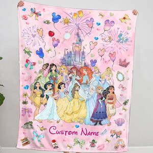 May include: Pink fleece blanket featuring a colourful illustration of Disney princesses, a castle, and fireworks. The blanket includes a custom name in the bottom centre.