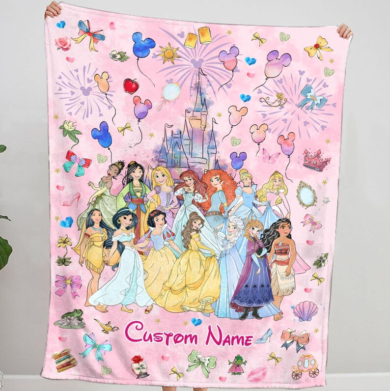 May include: Pink fleece blanket featuring a colourful illustration of Disney princesses, a castle, and fireworks. The blanket includes a custom name in the bottom centre.