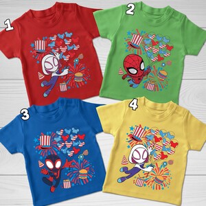 May include: Four short-sleeved t-shirts in red, green, blue, and yellow, each featuring a graphic print of a superhero character holding a bunch of balloons, a top hat, fireworks, and a burger, with numbered labels one through four.
