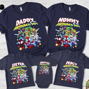 May include: A collection of navy blue t-shirts and a baby bodysuit featuring a graphic print of various superhero characters. The shirts display text including Daddy of the Birthday Boy, Mommy of the Birthday Boy, Sister of the Birthday Boy, Brother of the Birthday Boy, and Percy of Amazing Friends.