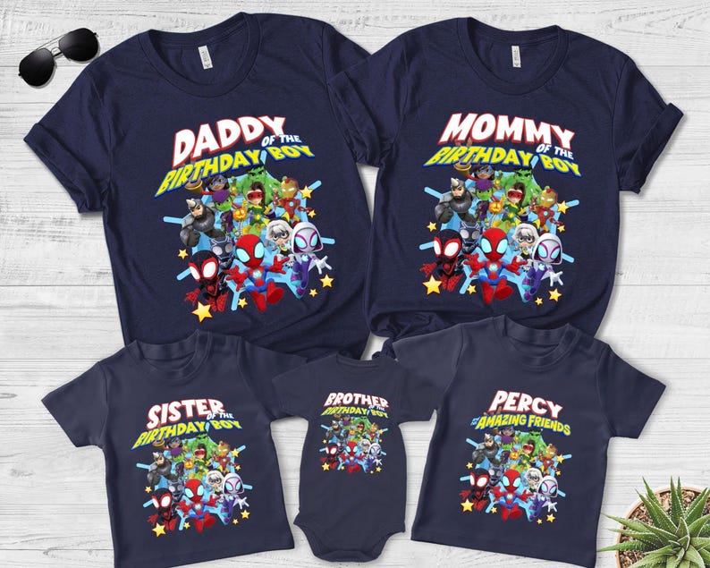 May include: A collection of navy blue t-shirts and a baby bodysuit featuring a graphic print of various superhero characters. The shirts display text including Daddy of the Birthday Boy, Mommy of the Birthday Boy, Sister of the Birthday Boy, Brother of the Birthday Boy, and Percy of Amazing Friends.