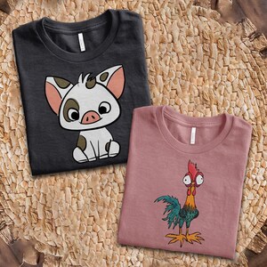 Puede incluir: Una camiseta gris oscuro con el gr&aacute;fico de un lech&oacute;n blanco con manchas marrones y orejas rosas, junto a una camiseta rosa polvoriento con el gr&aacute;fico de un gallo colorido con ojos grandes, cresta roja y plumas de cola verdes y azules.