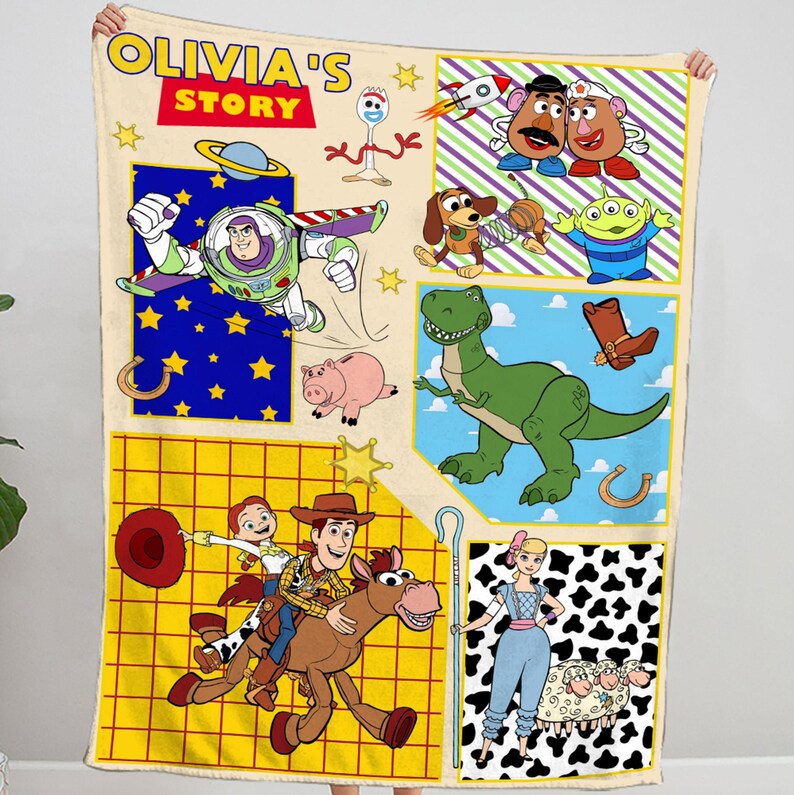 Puede incluir: Una manta colorida con personajes de la franquicia Toy Story. La manta tiene un fondo amarillo con un patr&oacute;n de cuadr&iacute;cula y presenta personajes como Woody, Buzz Lightyear, Rex y Jessie. La manta tambi&eacute;n incluye el texto "Olivia's Story".