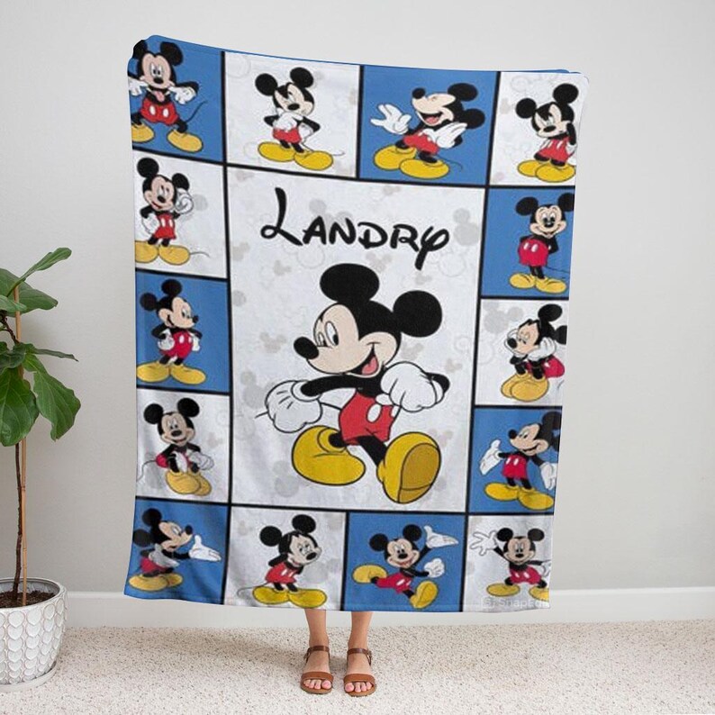 Puede incluir: Una manta azul y blanca con m&uacute;ltiples im&aacute;genes de Mickey Mouse en varias poses. La manta tiene un panel central con una imagen grande de Mickey Mouse y el nombre "Landry".