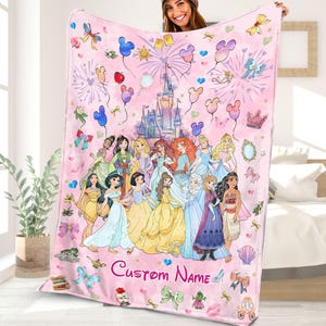 May include: Pink fleece blanket featuring a colourful illustration of Disney princesses in front of Cinderella's castle. The blanket has a pink background with hearts, stars and balloons. The text "Custom Name" is printed at the bottom of the blanket.