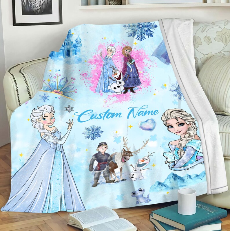 May include: A blue and white fleece blanket with a Frozen theme. It features Elsa, Anna, Olaf, and Sven. The blanket has a custom name field that says "Custom Name".