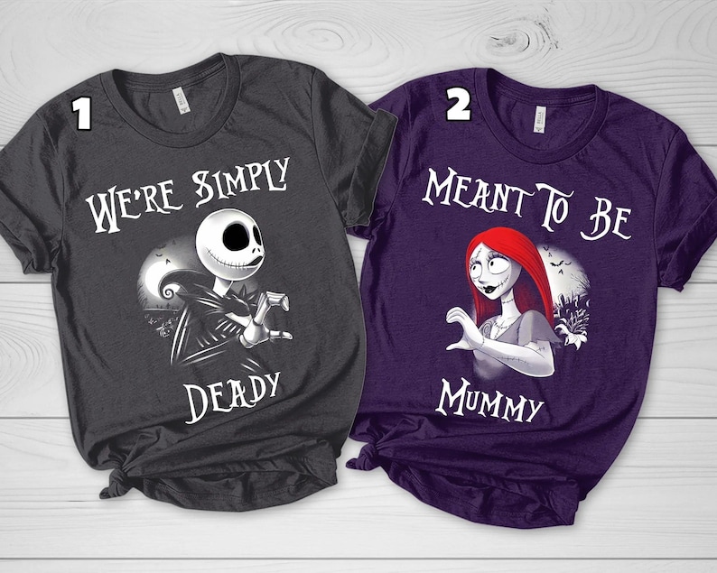 Puede incluir: Dos camisetas de manga corta, una gris oscuro y otra morada, con estampados gr&aacute;ficos de personajes. La camiseta gris muestra un personaje esqueleto con el texto "WE'RE SIMPLY DEADY", mientras que la morada muestra un personaje de pelo rojo con "MEANT TO BE MUMMY."