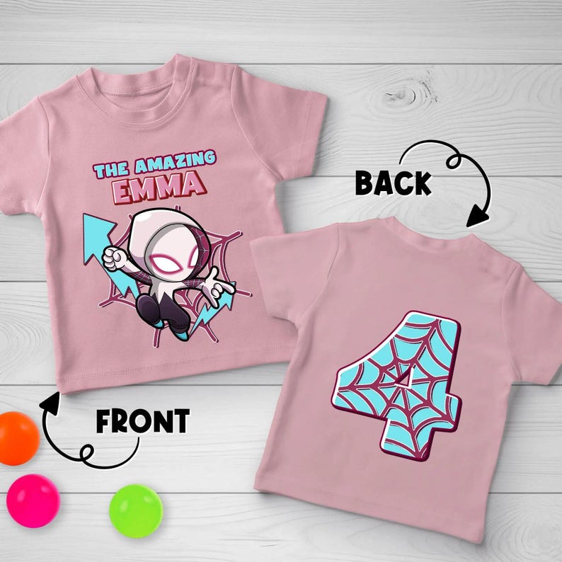 May include: A light pink t-shirt featuring a cartoon character in a white and purple suit with the text THE AMAZING EMMA on the front, and a second light pink t-shirt displaying a large number 4 with a blue and red spiderweb pattern on the back.