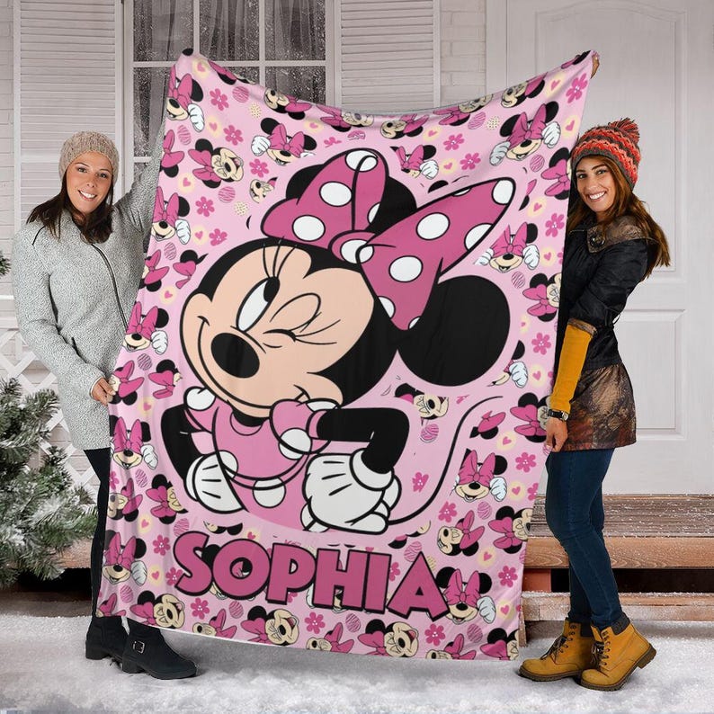 May include: Pink fleece blanket featuring Minnie Mouse with a large polka dot bow. The blanket has a repeating pattern of Minnie Mouse and hearts. The name "SOPHIA" is printed in pink. A cosy and colourful blanket.