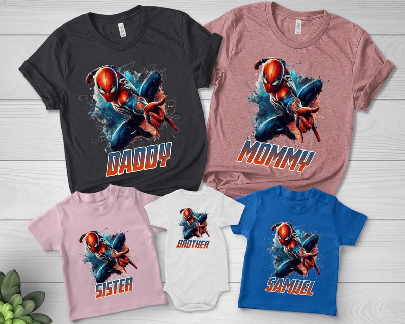 May include: A collection of five t-shirts and one bodysuit featuring a graphic of a red and blue superhero in a dynamic pose. The shirts are black, mauve, light pink, white, and blue, with the text DADDY, MOMMY, SISTER, BROTHER, and SAMUEL.
