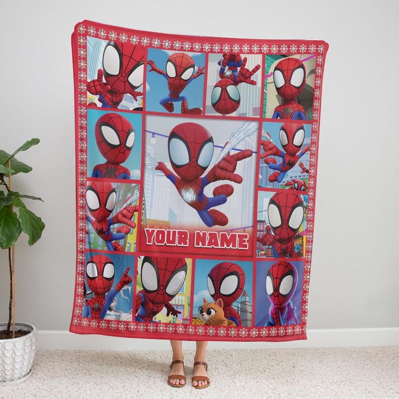 Pu&ograve; includere: Coperta rossa con pi&ugrave; immagini di Spider-Man in un motivo a griglia. La coperta ha un bordo rosso con un motivo a fiocco di neve e il testo "YOUR NAME". La coperta &egrave; tenuta da una persona.