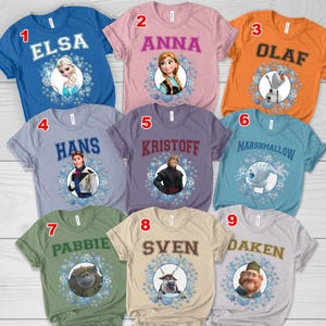 May include: Nine short-sleeved t-shirts in various colors, each featuring a character from the movie Frozen. The shirts display names like Elsa, Anna, Olaf, Hans, Kristoff, Marshmallow, Pabbie, Sven, and Oaken, with snowflake graphics.