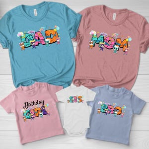 May include: A collection of five t-shirts and one bodysuit in various colors including teal, mauve, light pink, white, and light blue. Each garment features colorful block lettering spelling DAD, MOM, BIRTHDAY GIRL, SIS, and BRO with cartoon characters.