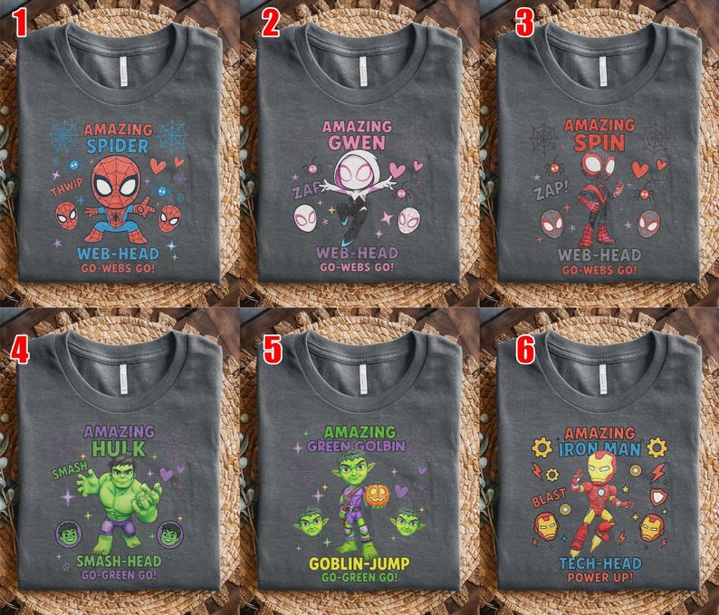 May include: A collection of six dark grey t-shirts featuring cartoon superhero graphics. Each shirt displays a character with text including Amazing Spider, Amazing Gwen, Amazing Spin, Amazing Hulk, Amazing Green Golbin, and Amazing Iron Man.