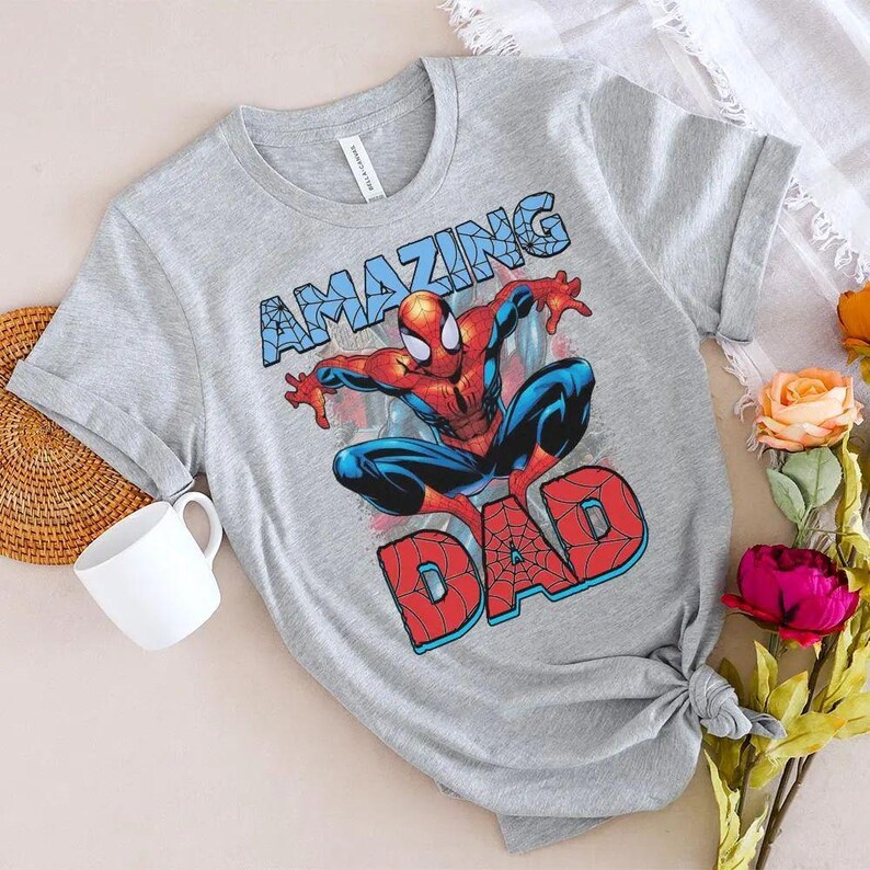 Pu&ograve; includere: Una t-shirt grigio melange a maniche corte con una grafica del supereroe Spider-Man in posa accovacciata. Sopra il personaggio c'&egrave; la parola AMAZING in blu, e sotto la parola DAD in rosso, entrambe con un design a motivo di ragnatela.