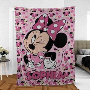 May include: Pink Minnie Mouse blanket featuring a large image of Minnie winking, wearing a polka dot bow and dress. The blanket has a repeating pattern of Minnie Mouse and flowers. The name "SOPHIA" is printed in large pink letters.
