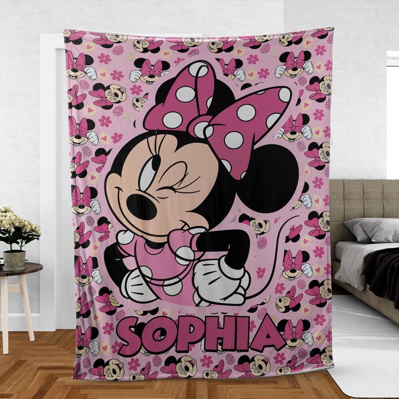May include: Pink Minnie Mouse blanket featuring a large image of Minnie winking, wearing a polka dot bow and dress. The blanket has a repeating pattern of Minnie Mouse and flowers. The name "SOPHIA" is printed in large pink letters.
