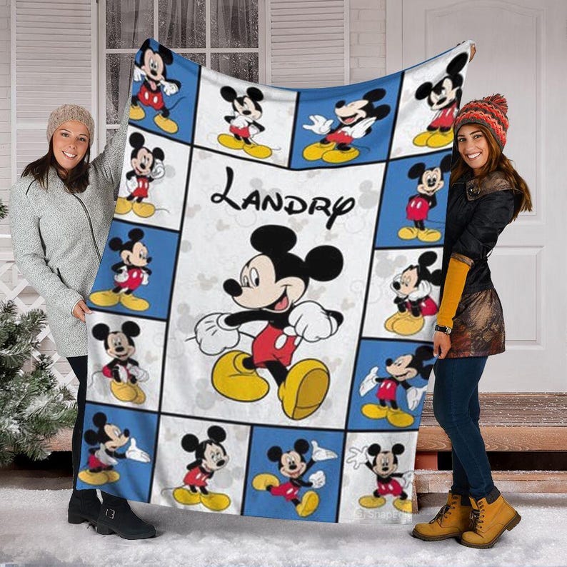 Puede incluir: Una manta rectangular grande con un patr&oacute;n repetido de Mickey Mouse en varias poses sobre un fondo azul y blanco. El nombre "Landry" est&aacute; impreso en escritura negra. La manta est&aacute; sostenida por dos personas.