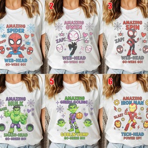 May include: A collection of six white t-shirts featuring cartoon superhero graphics. Each shirt displays a character with themed text including Amazing Spider Web-Head, Amazing Gwen Web-Head, Amazing Spin Web-Head, Amazing Hulk Smash-Head, Amazing Green Goblin Goblin-Jump, and Amazing Iron Man Tech-Head.