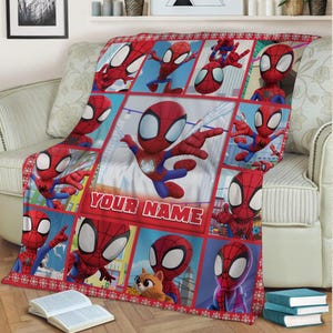 Pu&ograve; includere: Una coperta rossa e blu a tema Spider-Man con un motivo ripetuto del supereroe in varie pose. La coperta presenta il testo "YOUR NAME" in un riquadro rosso ed &egrave; bordata da un motivo a fiocco di neve rosso e bianco.