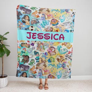 K&ouml;nnte beinhalten: Eine farbenfrohe Decke mit verschiedenen Zeichentrickfiguren in einem sich wiederholenden Muster. Die Decke hat ein hellblaues Band mit dem Namen "JESSICA" in rosa Buchstaben. Die Decke besteht aus weichem Material.