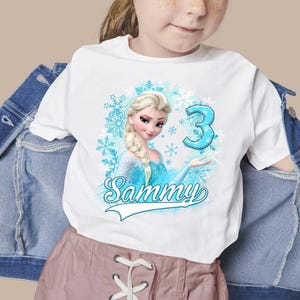 May include: A white t-shirt featuring a graphic of a blonde character with a braid in a blue dress, surrounded by light blue snowflakes. The design includes the large blue number 3 and the name Sammy in a cursive script font below the character.