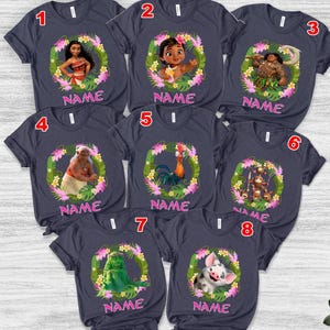 May include: Eight dark gray short-sleeve t-shirts featuring various Moana character graphics inside floral and leaf wreaths. Each shirt includes the word NAME in pink text below the graphic and a numbered red tag in the top corner.