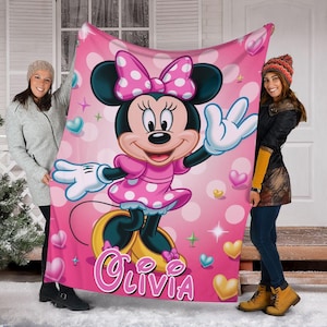 Puede incluir: Una manta rosa con Minnie Mouse con un vestido de lunares y un lazo. La manta tiene un fondo rosa con corazones y estrellas. El nombre "Olivia" est&aacute; escrito en rosa en la parte inferior. La manta est&aacute; sujeta por dos personas.