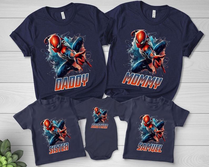 May include: A collection of five navy blue t-shirts and one bodysuit featuring a graphic of a red and blue superhero in a dynamic pose. Each garment displays the character above text that reads DADDY, MOMMY, SISTER, BROTHER, or SAMUEL.
