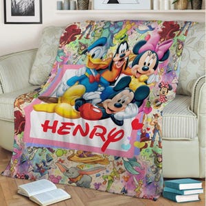 May include: A colorful Disney-themed blanket featuring Mickey Mouse, Minnie Mouse, Donald Duck, and Goofy. The blanket has a pink border with the name "HENRY" in red. The background is filled with various Disney characters and elements.