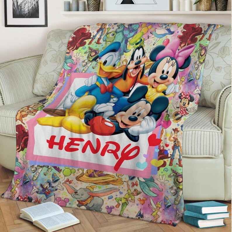 May include: A colorful Disney-themed blanket featuring Mickey Mouse, Minnie Mouse, Donald Duck, and Goofy. The blanket has a pink border with the name "HENRY" in red. The background is filled with various Disney characters and elements.