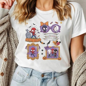 May include: A white t-shirt featuring a colorful Halloween-themed graphic with cartoon characters including Spider-Man, Ghost-Spider, and Miles Morales. The design includes pumpkins, bats, spiderwebs, and text that reads SPIDEY AND AMAZING SPIDERMAN.