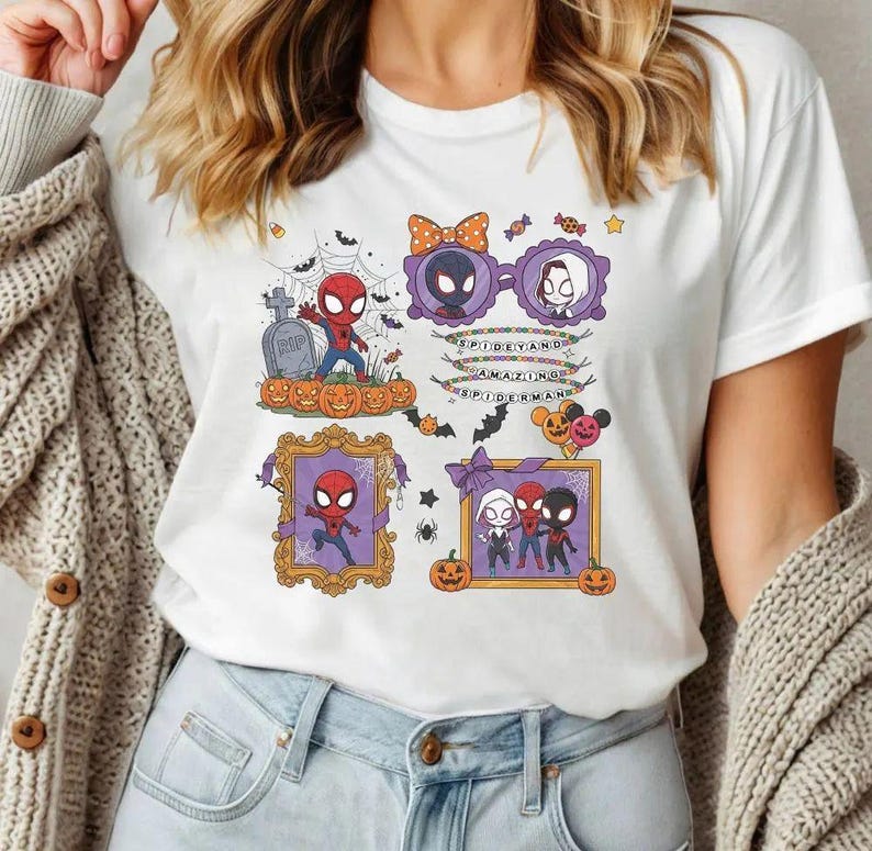 May include: A white t-shirt featuring a colorful Halloween-themed graphic with cartoon characters including Spider-Man, Ghost-Spider, and Miles Morales. The design includes pumpkins, bats, spiderwebs, and text that reads SPIDEY AND AMAZING SPIDERMAN.