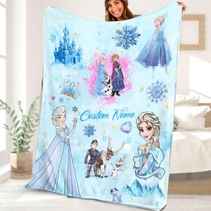 May include: A blue fleece blanket with a Frozen theme. It features images of Elsa, Anna, Olaf, and other characters from the movie. The blanket has a white background with snowflakes and a castle in the background. The text "Custom Name" is printed on the blanket.