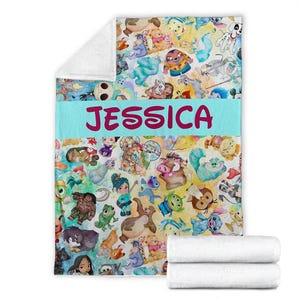 K&ouml;nnte beinhalten: Eine farbenfrohe Decke mit verschiedenen Zeichentrickfiguren. Die Decke hat ein hellblaues Band mit dem Namen "JESSICA" in rosa Buchstaben. Die Decke ist mit zwei wei&szlig;en Handt&uuml;chern gefaltet.