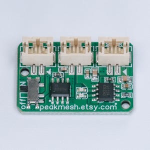 May include: A rectangular green printed circuit board featuring three white plastic connectors along the top edge, a small silver sliding switch on the left, and two black integrated circuit chips. The text peakmesh.etsy.com is printed in white.