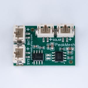 May include: A green rectangular printed circuit board module featuring four white JST-style connectors, two black integrated circuit chips, and various surface-mount components. The board is labeled with PeakMesh, SYS, BAT, and SOLAR text.