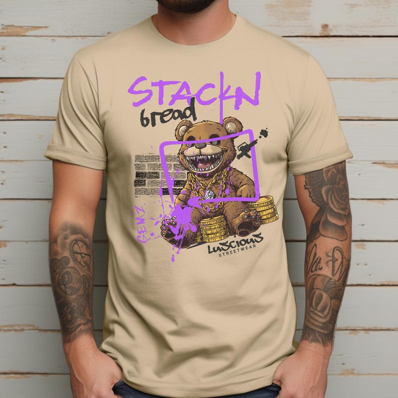 Stackin Bread Teddy Graphic T-Shirt in Sand featuring a bold teddy bear design with vibrant purple accents. This trendy streetwear shirt is perfect for men and women who love urban fashion. Made with soft fabric for all-day comfort and bold style.